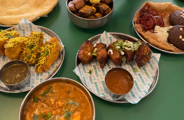 Original photo of Indian street food, fried snacks, patties, curry, flatbread and dipping sauces on metal dishes at Bundobust.