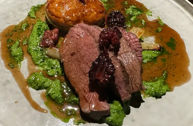 Original photo of sliced venison with blackberries, a round pastry, vegetables and sauce on a ceramic plate at Manifest.